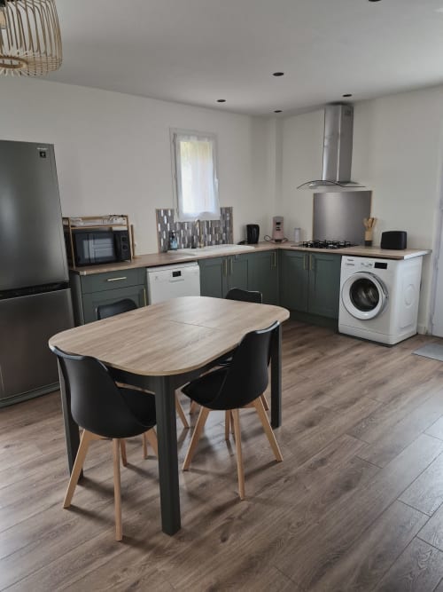 Cocina y comedor de cabaña moderna en Domaine en Terre Happy con mesa de madera, sillas negras y electrodomésticos de acero inoxidable