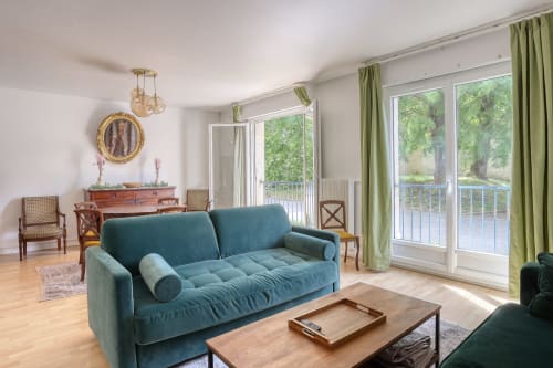 Canapé turquoise dans le salon du Versailles Luxury Retreat avec vue sur le jardin, mobilier en bois et grandes portes vitrées donnant sur le parc