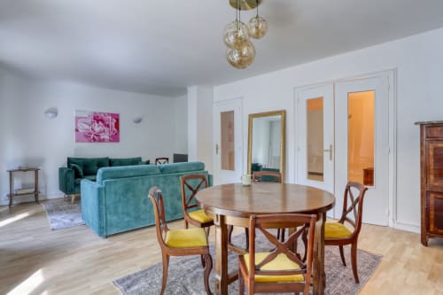 Spacieuse retraite de luxe à Versailles avec table à manger, sièges turquoise, lustres suspendus et portes donnant sur le jardin