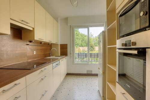 Cuisine moderne aux armoires crème et plan de travail en bois, vue sur le jardin par les portes du balcon au Versailles Luxury Retreat.