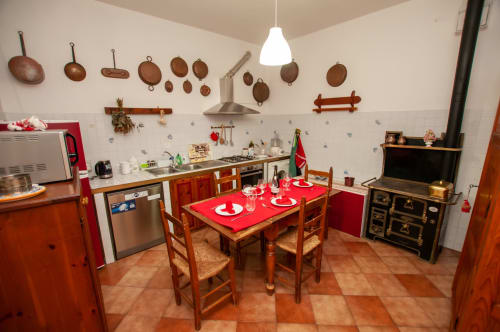Rustic Italian kitchen at Cristallo Apartment in Ravenna with red dining table, copper pans, and vintage stove.