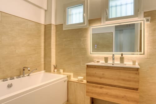Salle de bains luxe moderne à Versailles Retreat avec vanité en bois, miroir éclairé, baignoire et carrelage chaleureux