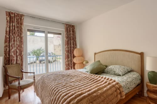 Chambre élégante avec vue sur le jardin au Versailles Luxury Retreat, lit en bois, rideaux à fleurs rouges et accès au balcon.