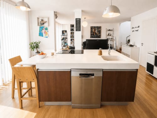 Cocina moderna con encimeras blancas, carpintería de madera, isla central y electrodomésticos de acero inoxidable en primera línea de playa América