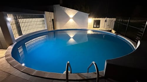 Piscina ovalada iluminada en los Apartamentos Voramar de Cambrils con iluminación moderna y servicios junto a la piscina por la noche