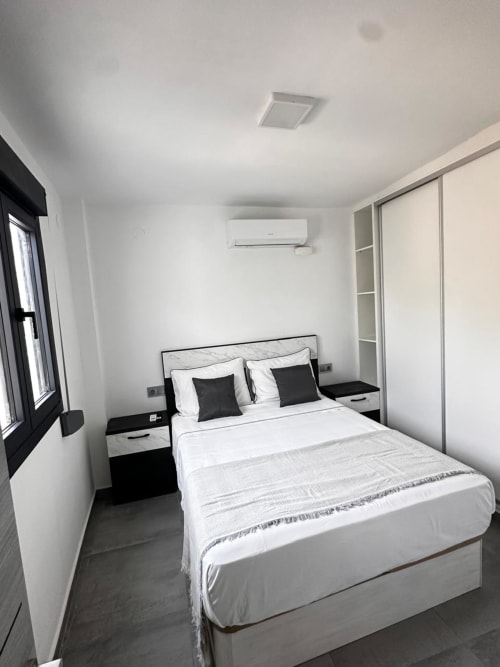 Dormitorio moderno en villa Apartaments Voramar en Cambrils con cama de matrimonio, mesillas negras, paredes blancas y aire acondicionado