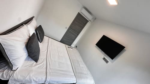 Dormitorio moderno de la villa Apartaments Voramar en Cambrils con cama blanca, almohadas oscuras, TV de pantalla plana y aire acondicionado