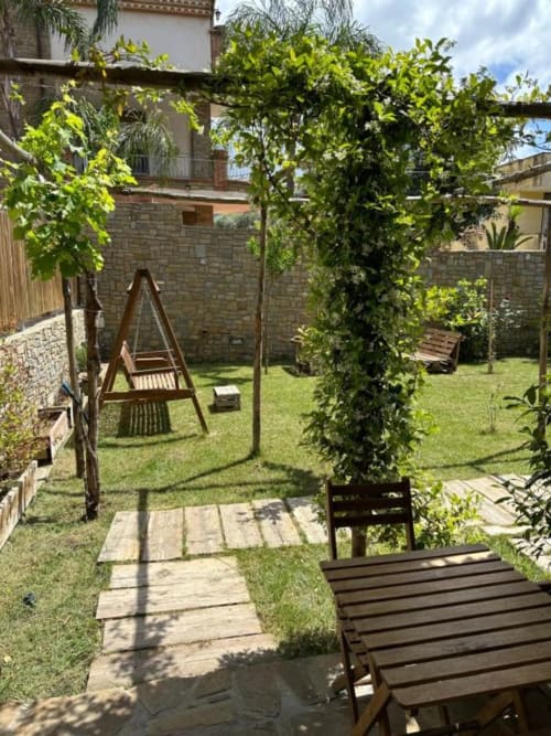 Lussureggiante giardino alle Cilento Rooms ad Agnone con pergolato in legno, sedie sdraio, percorso in pietra e muri in laterizio
