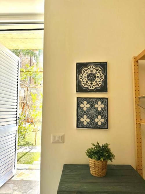 Muro giallo con due opere d'arte in piastrelle decorative nere e beige, pianta in vaso su tavolo, vista del giardino attraverso porta aperta