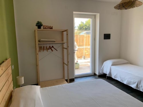 Camera tripla luminosa a Cilento Rooms B&B ad Agnone con due letti, scaffalature in legno, accesso a patio con vista giardino e arredamento moderno