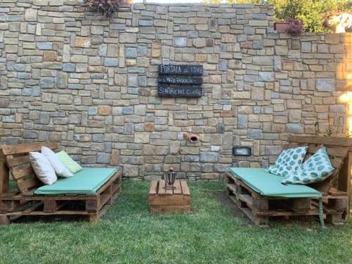 Angolo lounge con pallet e cuscini verde in giardino di Cilento Rooms, Agnone, rivolto verso muro in pietra con insegna con testo italiano.