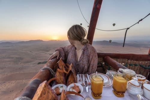 Femme dînant dans un panier de montgolfière au-dessus du désert de Marrakech à l'aube avec d'autres ballons visibles