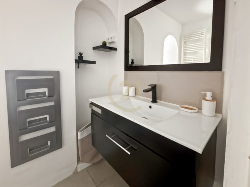 Salle de bains moderne à L'Île-Rousse avec vanité noire, lavabo blanc, miroir encadré et sèche-serviettes électrique