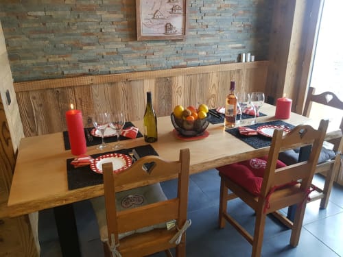 Salle à manger chaleureuse de l'appartement Zoppas Courchevel avec table en bois, bougies, vin, coupe de fruits et couverts pour un dîner intime