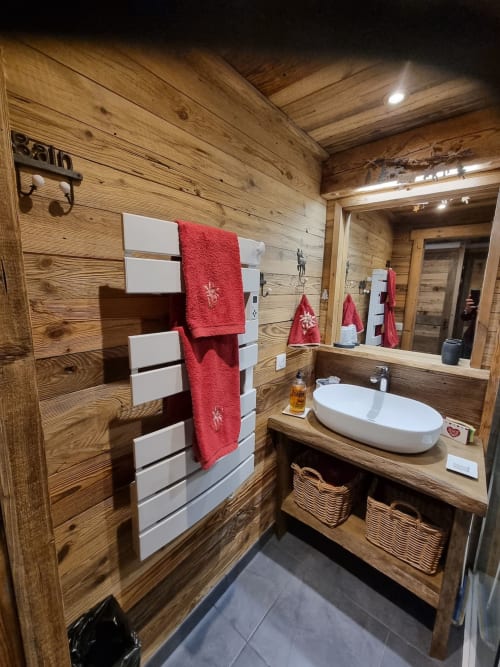 Salle de bain rustique en bois dans un appartement à Courchevel avec lavabo blanc, serviettes rouges et rangement.