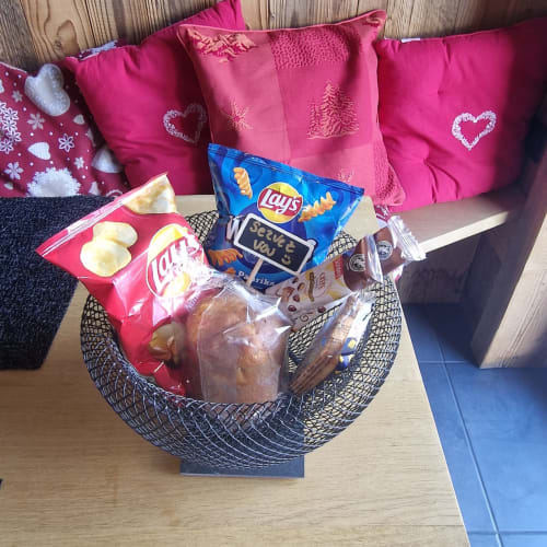 Panier de bienvenue cosy à Zoppas Courchevel avec gourmandises, friandises et coussins roses festifs sur table en bois