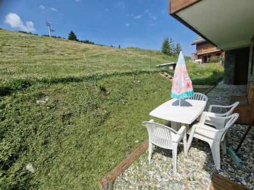 Mobilier de patio blanc et parasol coloré dominant les pentes verdoyantes de Zoppas Courchevel