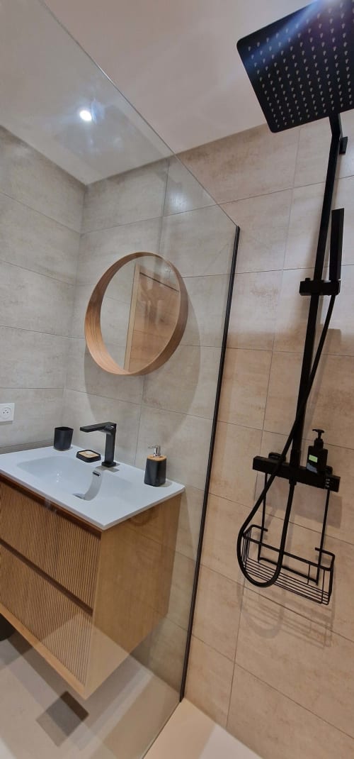 Salle de bain moderne avec miroir rond, pomme de douche pluie noire, vasque blanche, meuble bois et carrelage neutre à Zoppas Aix