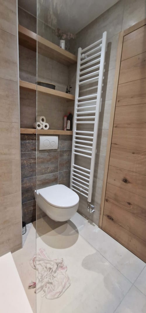 Salle de bain moderne avec toilettes murales, porte-serviettes blanc et touches de bois à l'appartement Zoppas Aix Les Bains