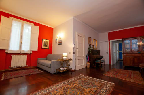 Bright red-walled living room in Cristallo Apartment, Ravenna, with gray armchair and wooden floors