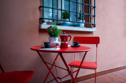 Bright red bistro table and chairs with flowers on a pink patio at Cristallo Apartment, Ravenna
