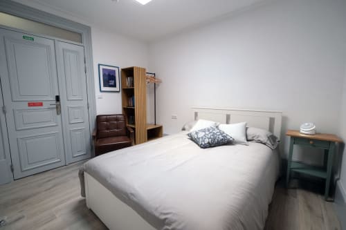 Quarto moderno no Santiago de Caminha Boutique Hostel com cama branca, criado verde, prateleiras em madeira e acabamento em madeira clara