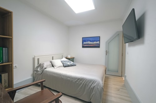 Quarto moderno na Santiago de Caminha Boutique Hostel com cama queen, TV de parede, prateleiras de madeira e claraboia luminosa
