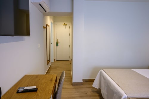 Habitación moderna del hotel Alcazaba Salobreña con suelo de madera, cama, escritorio y pasillo hacia la puerta de entrada