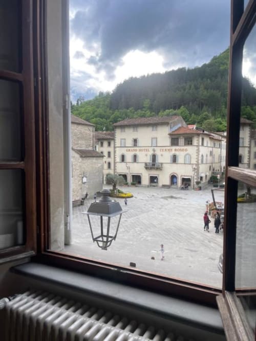 Grand Hotel Terme Roseo courtyard in Bagno di Romagna with forested mountains, historic buildings, and stone plaza