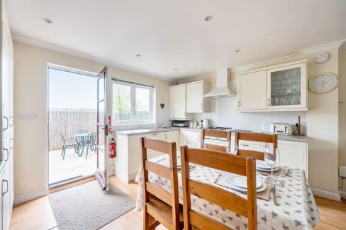 Bright kitchen and dining area at 2 Doves Holiday Property in Exeter with wooden chairs, cream cabinets, and patio access