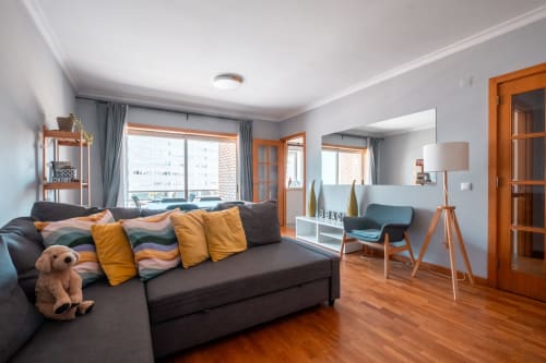 Sala de estar moderna no EcoHost em Perafita com sofá cinza-carvão, detalhes em laranja, assoalho de madeira, vistas da cidade