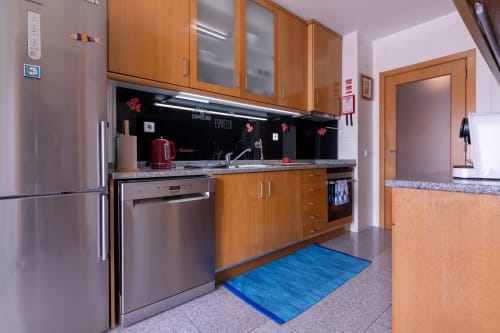 Cozinha moderna em apartamento EcoHost com armários de madeira, eletrodomésticos em aço inoxidável, bancada de granito e preto