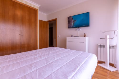Quarto moderno em rosa com vista oceânica, TV integrada, guarda-roupa em madeira, cômoda branca e piso de madeira na EcoHost Perafita