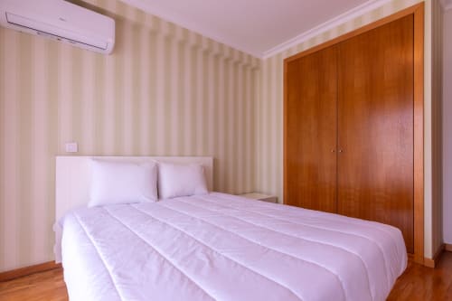 Quarto do apartamento OceanBreeze na EcoHost em Perafita com paredes listradas em rosa, guarda-roupa em madeira e vista para o mar