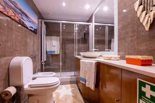 Banheiro moderno no apartamento OceanBreeze da EcoHost em Perafita, com chuveiro de vidro, pia, vaso sanitário e paredes em azulejos marrom.