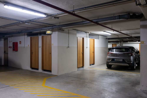 Garagem de estacionamento coberta no EcoHost em Perafita com marcações em linhas amarelas, salas de utilitários e veículo estacionado
