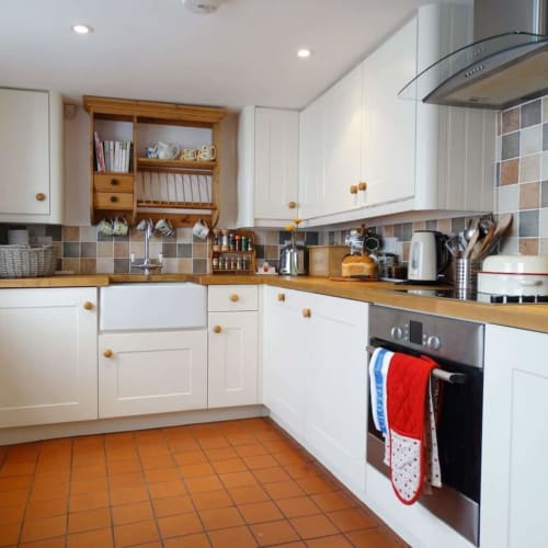 Bright kitchen at 2 Doves Holiday Property in Exeter with white cabinets, wooden worktops, terracotta tiles, and modern