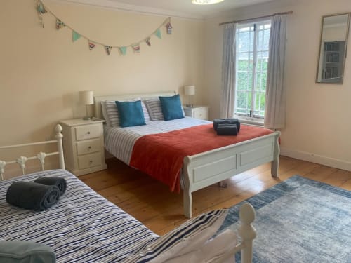 Bright bedroom at 2 Doves Holiday Property, Exeter with two beds, white furniture, blue pillows and red throw.
