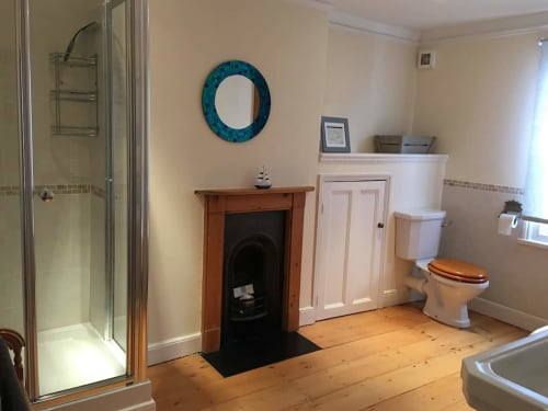 Spacious bathroom at 2 Doves Holiday Property in Exeter with wooden flooring, fireplace, shower, toilet, and teal mirror.