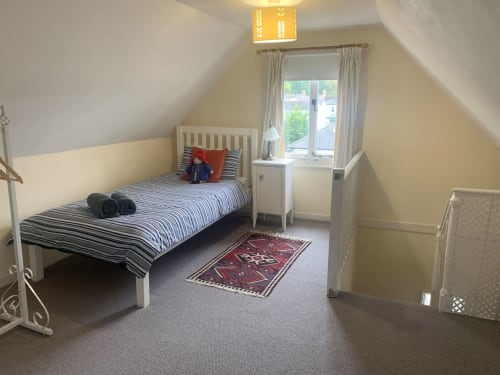 Bright attic bedroom at 2 Doves Holiday Property, Exeter with single bed, striped bedding, window, and red patterned rug