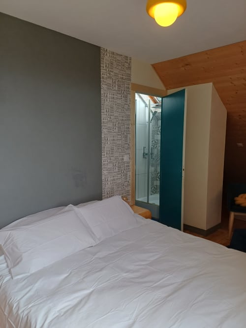 Modern bedroom at La Maison de Dun B&B with white bed, gray wall, patterned accent panel, and ensuite shower, Saint Racho