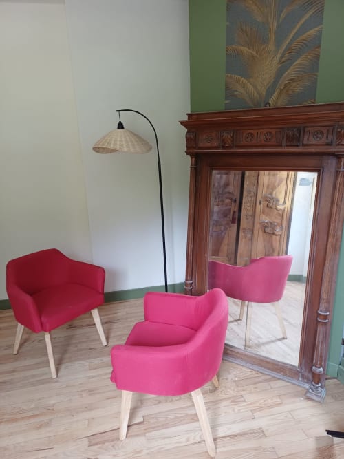 Modern lounge seating area at La Maison de Dun with pink and red armchairs, arc lamp, wooden fireplace, and garden view.