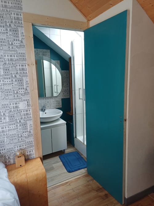 Modern bathroom entrance at La Maison de Dun BnB with teal accents, white sink, and mountain views in Chambre Soleil Bleu