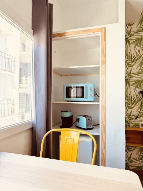 Étagères ouvertes dans la chambre d'auberge Nanit Rooms avec micro-ondes rétro bleu, grille-pain et chaise jaune au bureau à Santa Eulalia, Ibiza