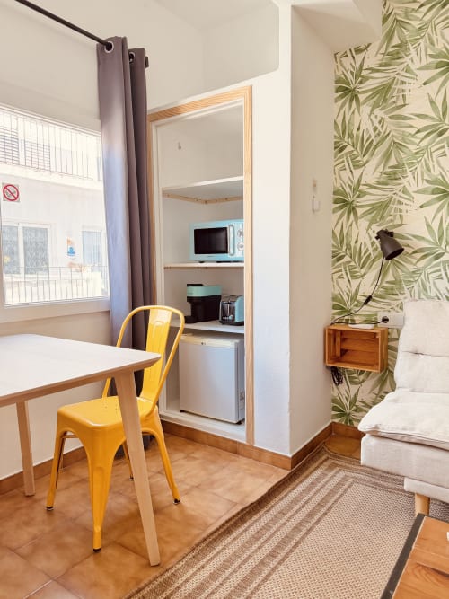 Chambre moderne à Nanit Rooms Ibiza avec chaise jaune, espace de travail, kitchenette et papier peint tropical