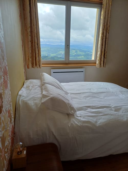 Bedroom with mountain views at La Maison de Dun B&B in Saint Racho, featuring white bedding and gold curtains overlooking