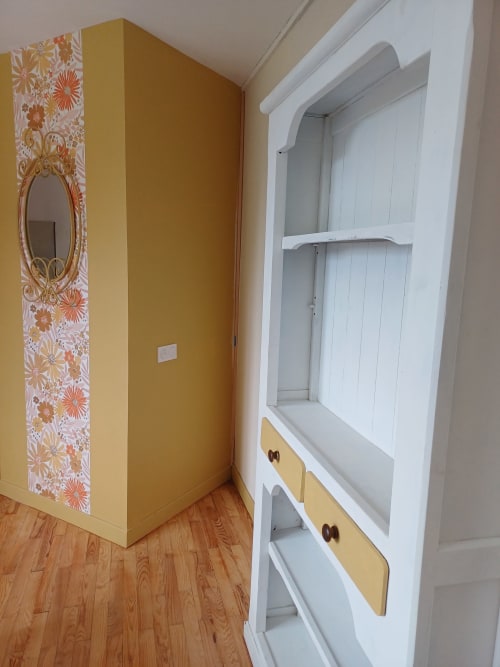 Chambre Passiflore at La Maison de Dun: white built-in shelving with yellow accents and wooden handles against mustard wall