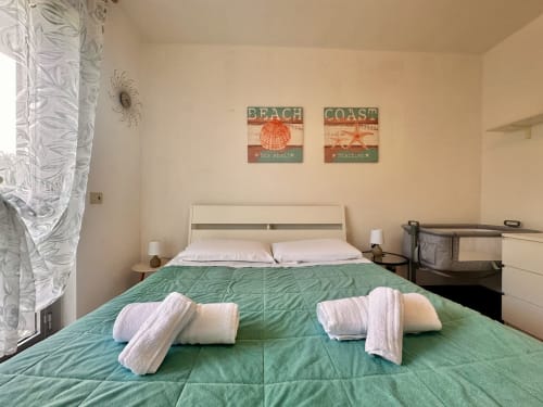Camera luminosa a Casa Sofia a Varigotti con letto trapuntato verde, cuscini bianchi, arte murale a tema costiero e design moderno