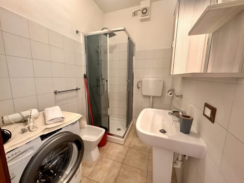 Bagno moderno dell'appartamento Casa Sofia a Varigotti. Dotato di doccia, lavandino, toilet, lavatrice e piastrelle bianche.