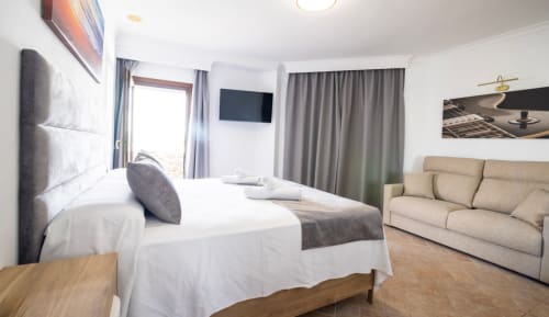 Amplia habitación triple en Boutique Zahara de los Atunes con cama doble, sofá, TV y balcón en Cádiz